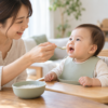 椅子で体を起こして離乳食を食べる赤ちゃんと母親（AI生成画像）