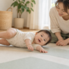 保護者がそばで見守る中、床のマットで体を横に向ける赤ちゃんのイメージ
