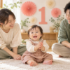 数字の1とコーラルピンクの飾りを背景に、1歳の子どもと両親が笑顔で座っている