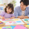 4歳ごろの女の子がクレヨンで絵を描き、隣で父親が笑顔で見守っている
