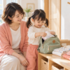 母親が見守る中、3歳ごろの子どもがタオルをバッグに入れて朝の支度をしている