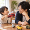 赤い車のおもちゃを持つ子どもの話を、父親が目線を合わせて聞く様子