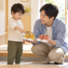 父親が黄色とコーラル色の靴を見せ、2歳ごろの子どもが黄色の靴を指さして選んでいる