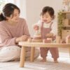 低いテーブルで積み木遊びをする幼児を見守る母親（AI生成イメージ）