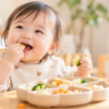 明るいダイニングで離乳食を手づかみして食べる生後9か月ごろの赤ちゃん