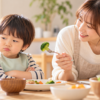 食卓でブロッコリーを嫌がる3歳ごろの男の子と、優しく声をかける母親
