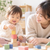 1歳くらいの女の子がお母さんと一緒に木製の積み木で遊んでいる様子
