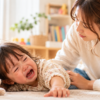 イヤイヤ期で泣いている2歳ごろの子どもに、優しく寄り添う母親
