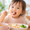 1歳くらいの女の子がスプーンを使って食事を楽しんでいる様子