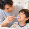 父親が3歳くらいの息子の仕上げ磨きをしている様子