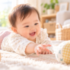 明るいリビングで布製のボールに手を伸ばして遊ぶ生後7か月ごろの赤ちゃん
